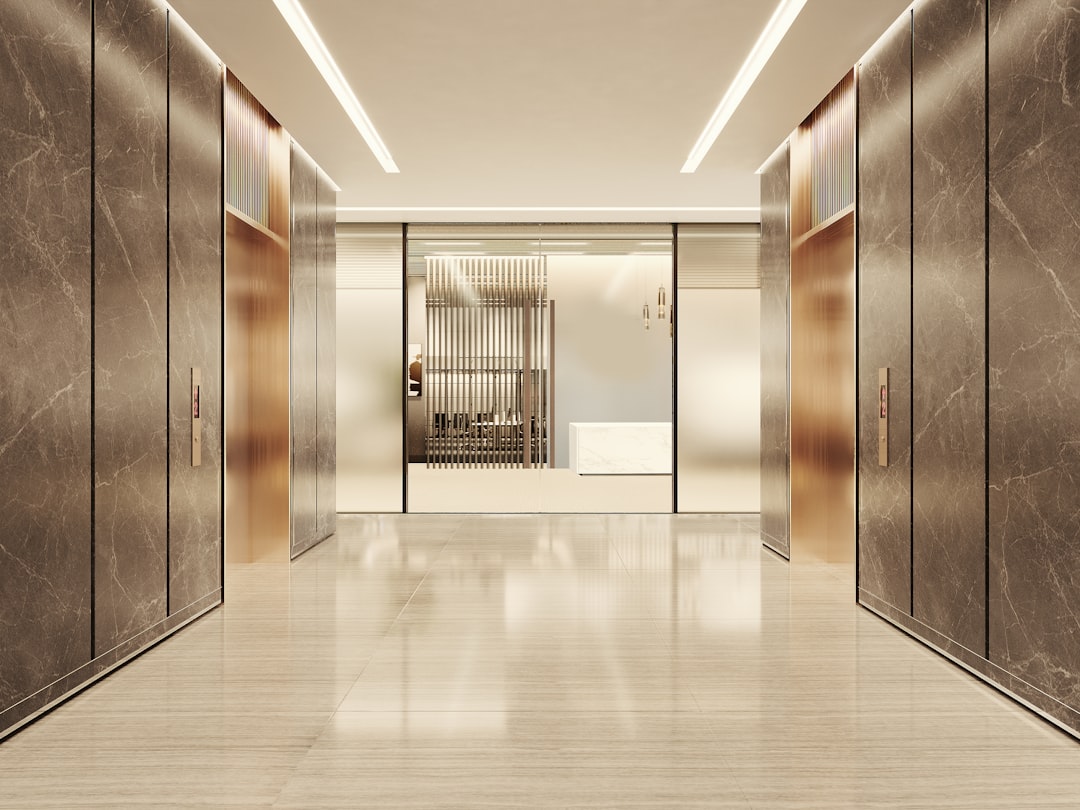 A sleek, upscale commercial lobby with a marble-tiled floor and walls. The space is illuminated by modern linear lighting, leading to frosted glass doors