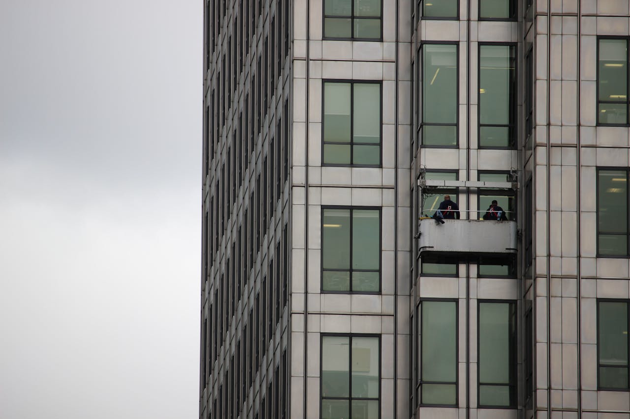 Two workers cleaning windows on a high-rise building facade in an urban environment.